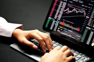 Bitunix A person types on a laptop keyboard with a crypto trading platform displayed on the screen, showing colorful stock charts, price data, and financial graphs against a dark background.