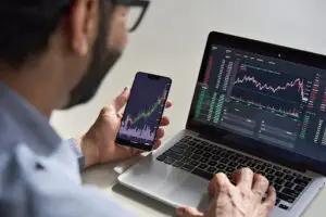 Bitunix A person looks at financial charts on a smartphone and a laptop, analyzing stock market data and crypto trading trends with colorful graphs and trading information displayed on the screens. | Bitunix crypto trading