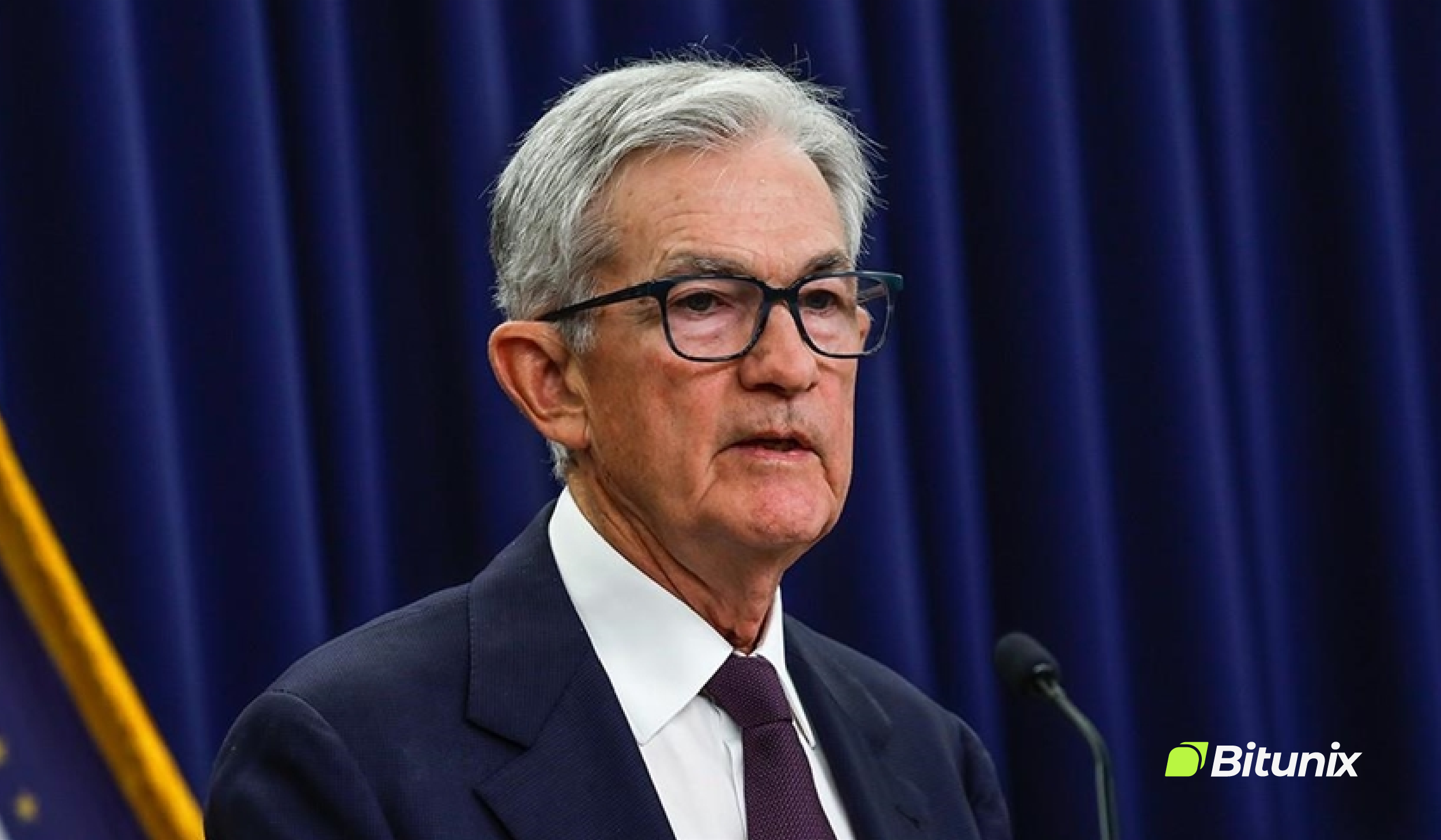 Jerome Powell, a senior Fed official, wears a dark suit, white shirt, and tie as he speaks at a podium in front of dark curtains. 